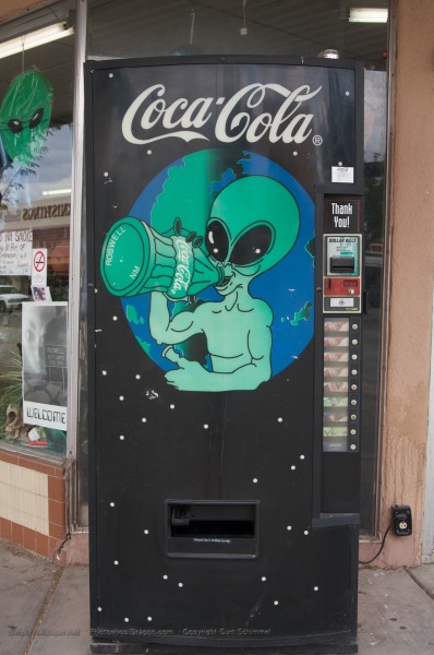 coke machine with signage depicting an alien drinking a coke
