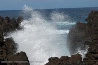 ocean wave crashing on shoreline of rough lava rocks